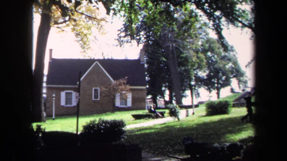 1970 Washington, DC home-movie view of a brick building and public green space framed by trees and shadowed film edges.