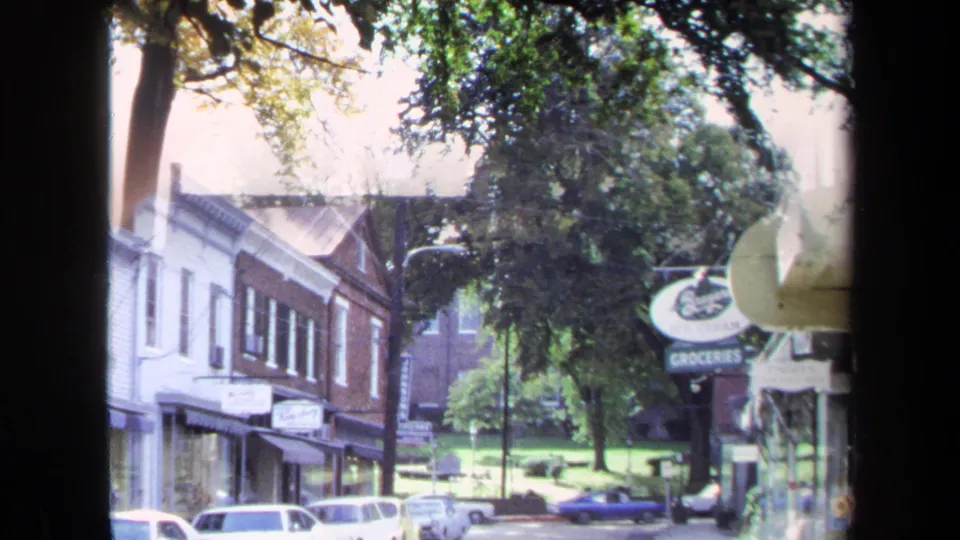 1970 Washington, DC street scene showing storefronts, parked cars, trees, and a visible groceries sign.