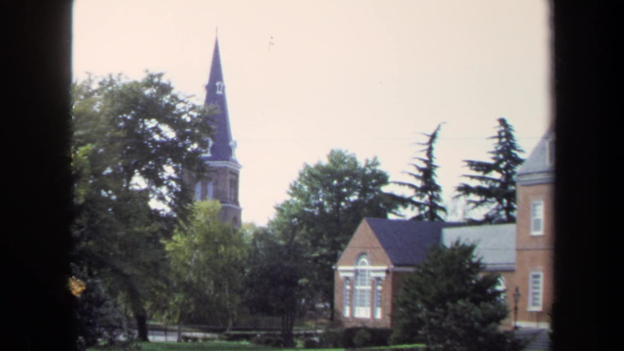 1970 Washington, DC 8mm frame showing brick buildings, trees, and a tall church steeple beyond dark window-like borders.