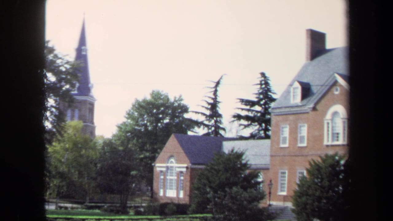 Washington, DC 1970 home-movie frame with red brick buildings, white-trimmed windows, trees, and a church steeple in the distance.