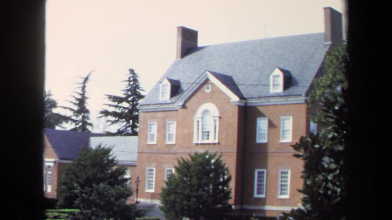 1970 Washington, DC home-movie frame showing a brick exterior building with dormers, trees, and heavy dark frame borders.