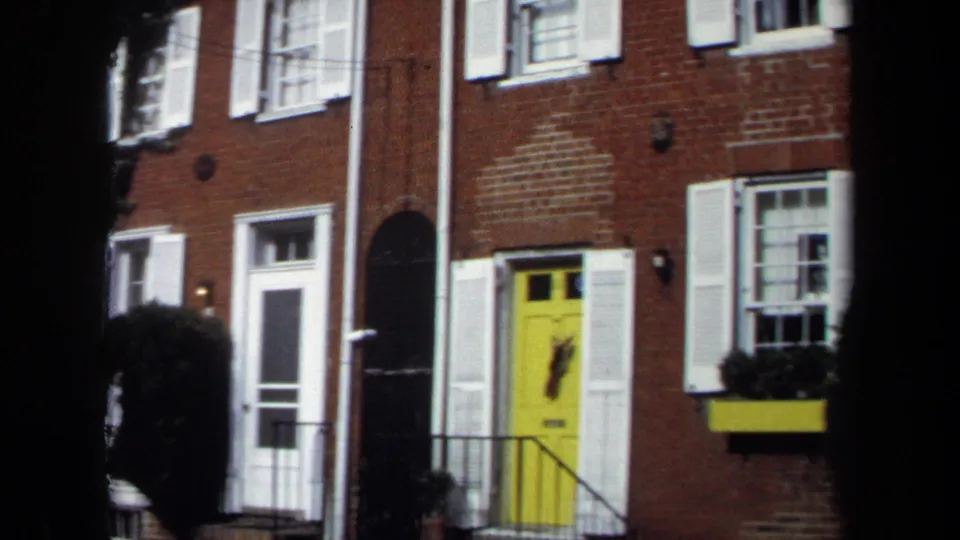 1970 Washington, DC view of brick row house fronts with yellow doors, white shutters, and a dark foreground band from the camera position.