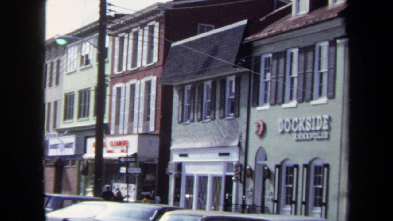 1970 Washington DC frame with the Dockside Annapolis sign visible on a light green building beside older storefronts and parked cars.