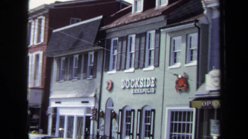 1970 Washington DC home-movie frame showing upper-story windows, storefront entrances, and the Dockside Annapolis facade during the pan.