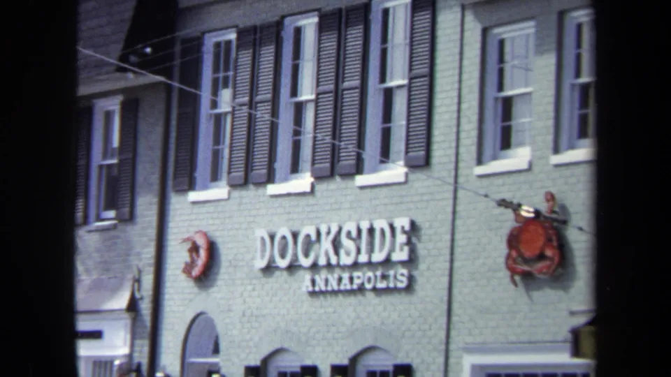 1970 Washington DC frame centered on the Dockside Annapolis sign, shuttered windows, painted brick, and crab decorations on the building facade.