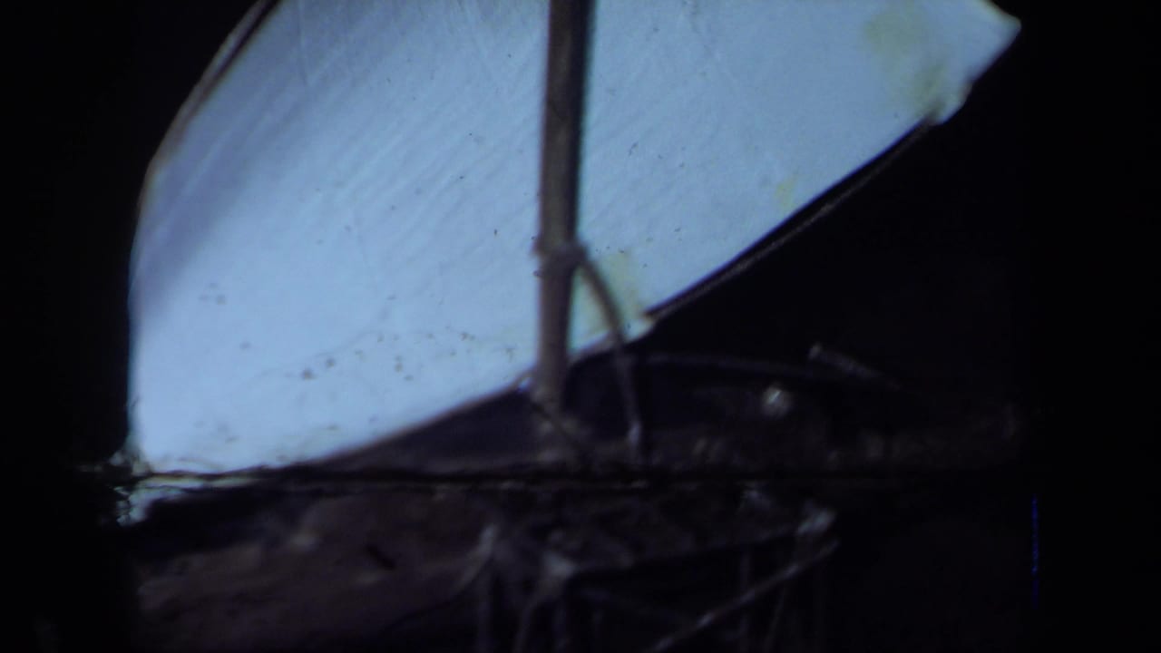 1971 California 8mm frame showing a dark tabletop with a pale sail-like form and partial pineapple centerpiece visible at the edge.