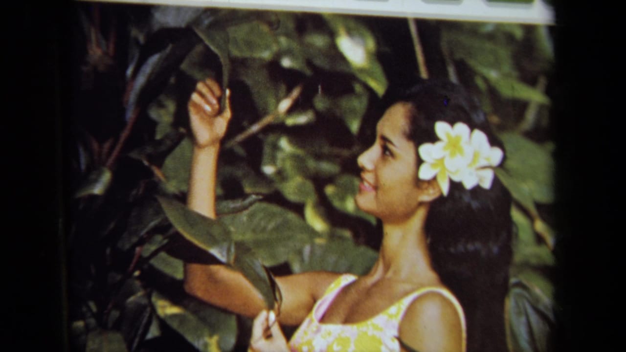 Woman with a white flower in her hair touches tropical leaves.