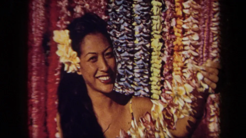 Tight 8mm frame of the poster or display image, with the woman smiling beside red, blue, yellow, and pink leis.