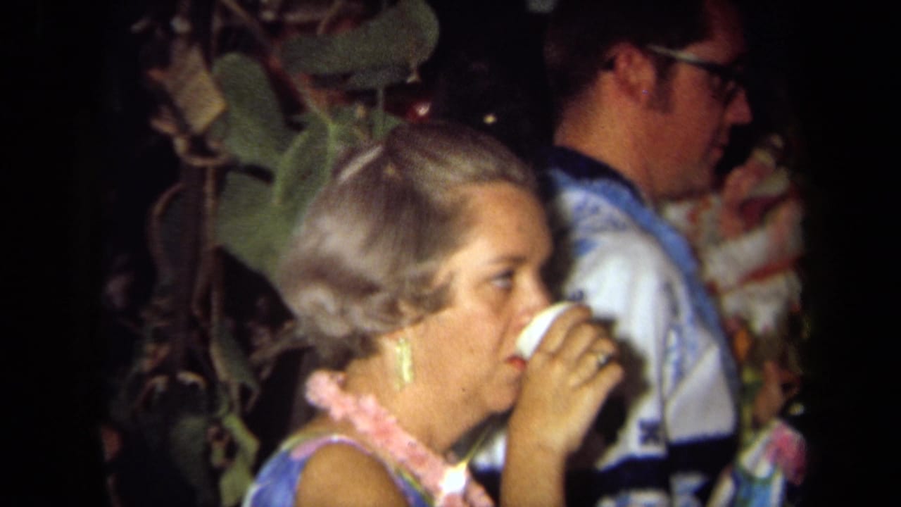 Woman wearing a pink lei drinks from a white cup beside guests in aloha-style clothing.