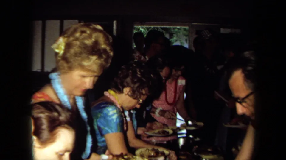 Guests in leis gather indoors with plates near a buffet table, matching the 1971 California social gathering metadata.