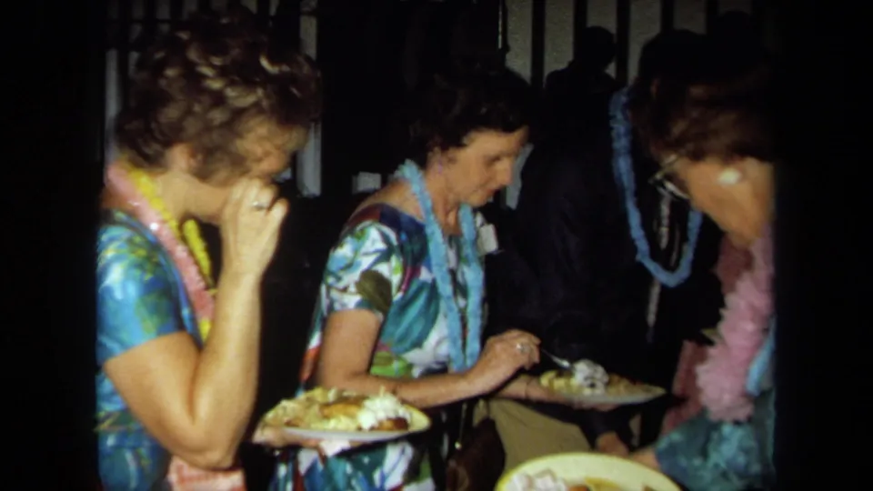 Candid 8mm frame of women in leis eating and holding plates during a 1971 California birthday party.