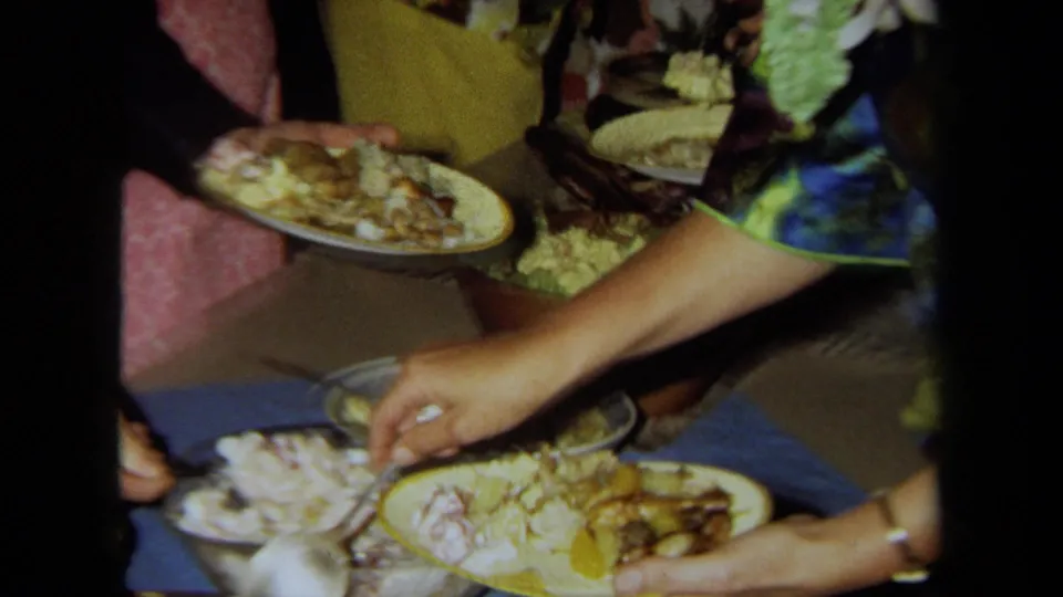 Guests' hands and plates fill the frame as food is served from communal dishes at the 1971 California party.