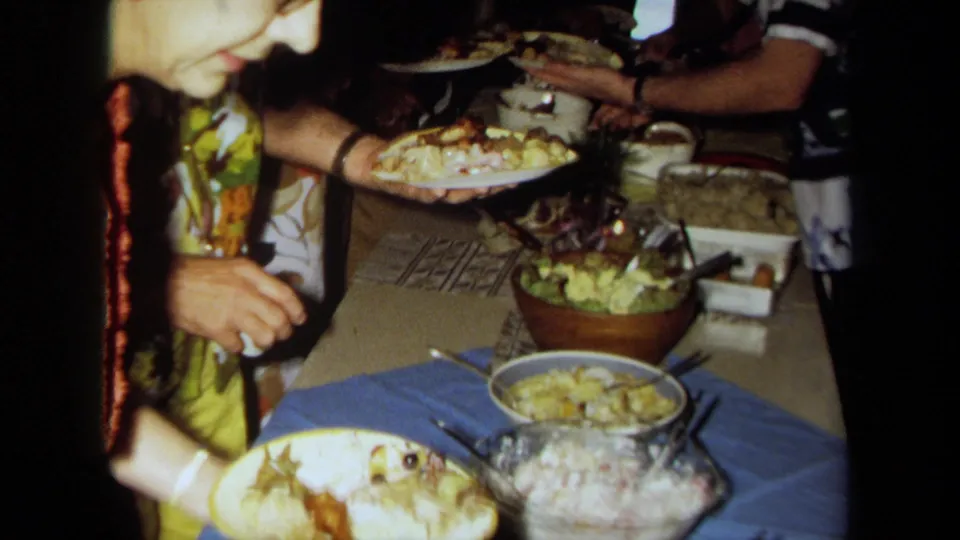 Close 1971 California home-movie view of a woman beside a buffet table with salad, serving dishes, plates, and folded cloths.