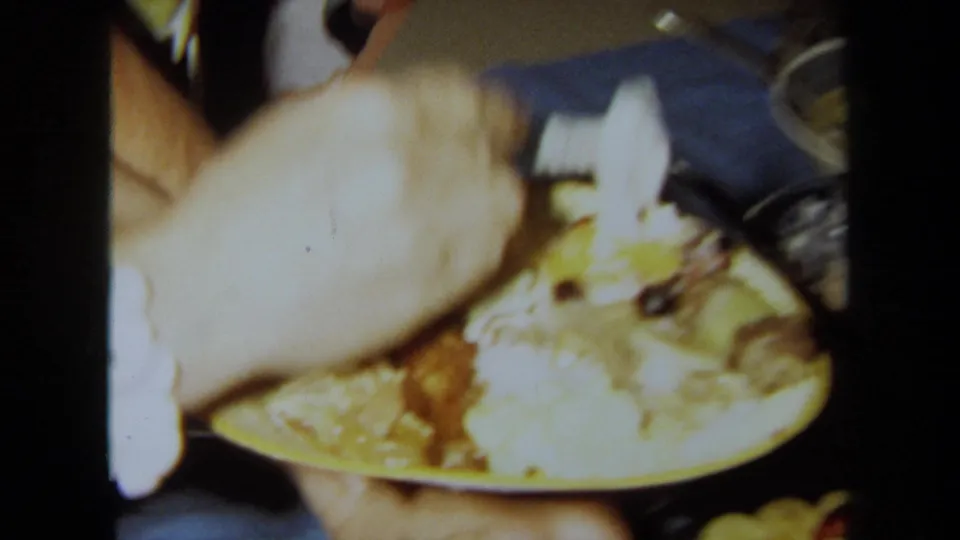 Soft, overexposed close-up from the 1971 California party showing a hand, a plate of food, and buffet items at very close range.