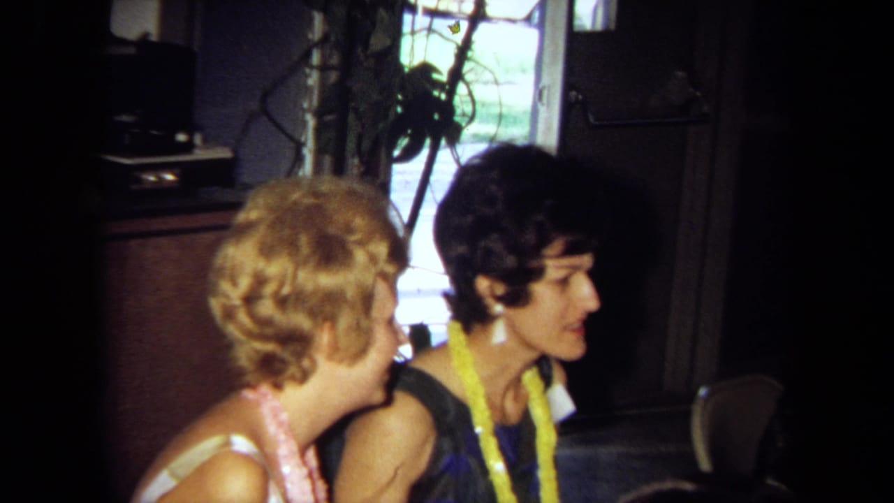 Two women in leis sit in profile near a window and dark wood furniture.