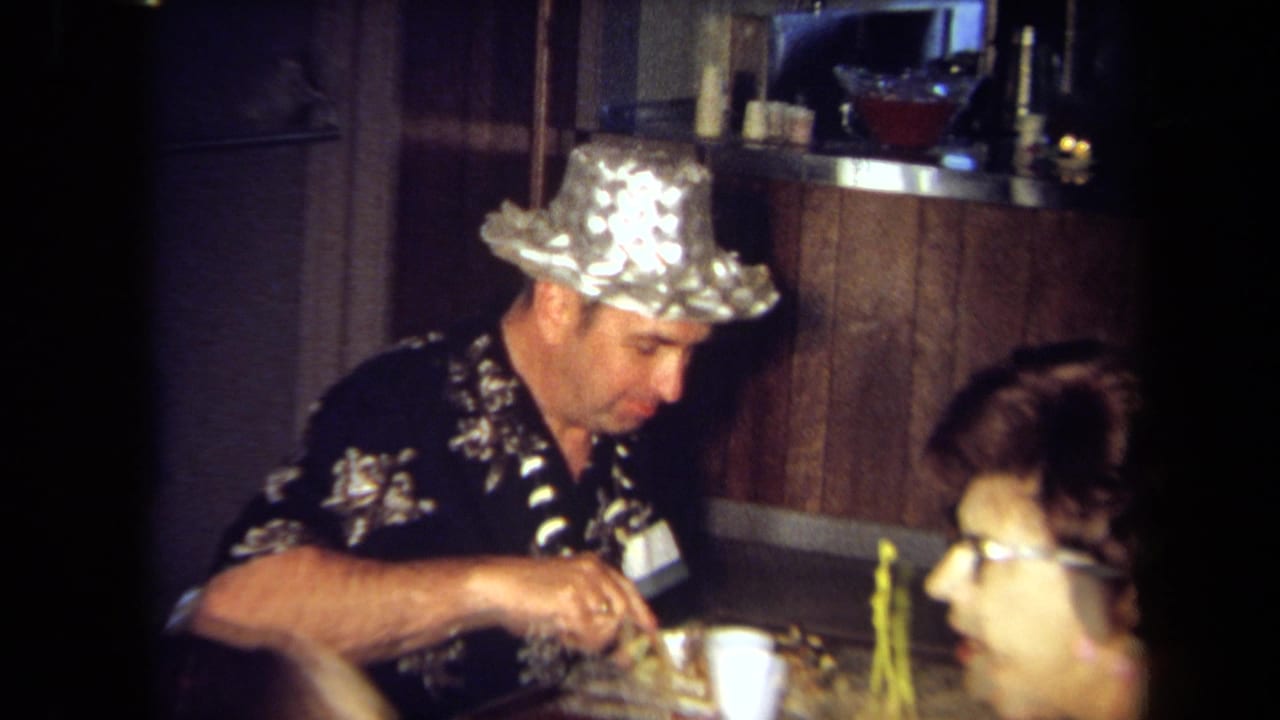 Man in a foil hat eats at a table beside another guest in a wood-paneled room.