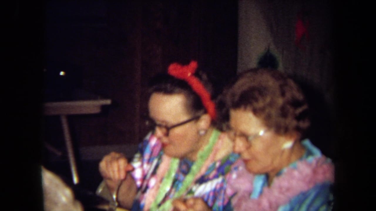 Two adults in colorful leis sit together at a table during the 1971 California family gathering.