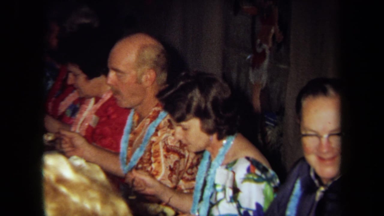 Adults in Hawaiian-style shirts and leis seated at a dim dinner table.