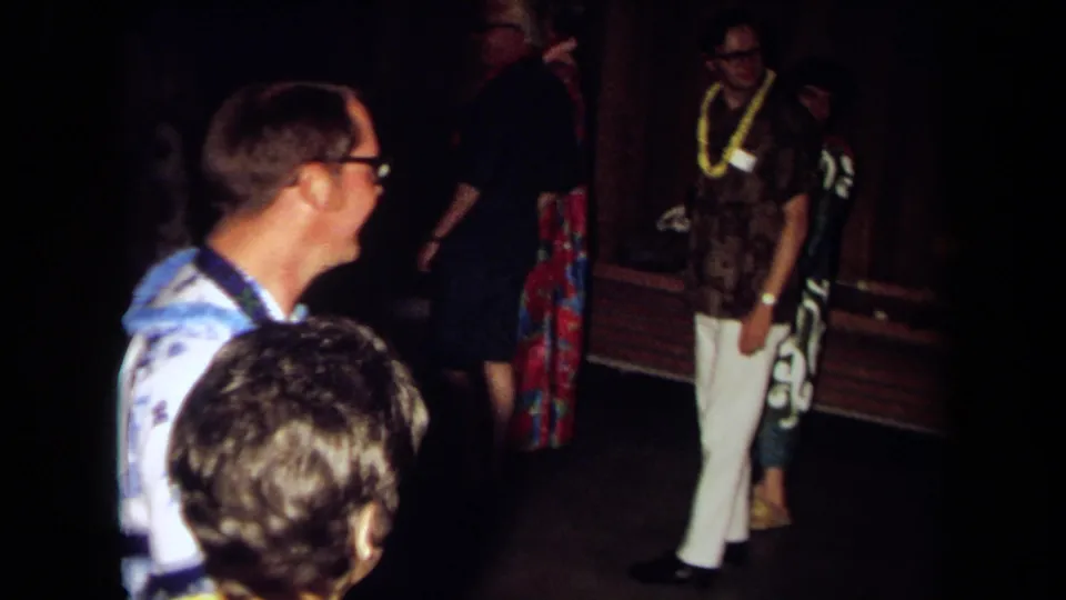 Adults in leis and aloha-style clothing gather inside a dim private room during the 1971 California party footage.