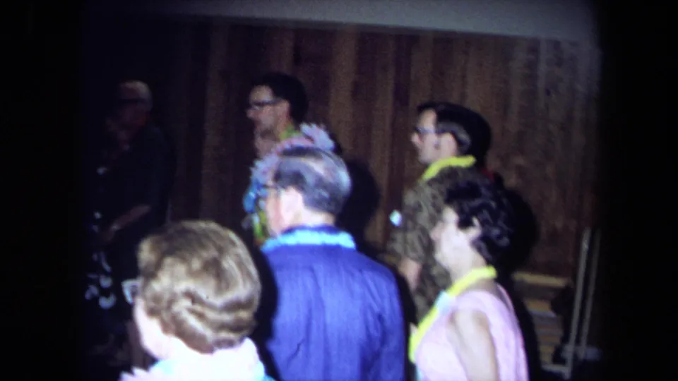 1971 California party footage with adults in leis and aloha-style clothing moving through a dim private interior.