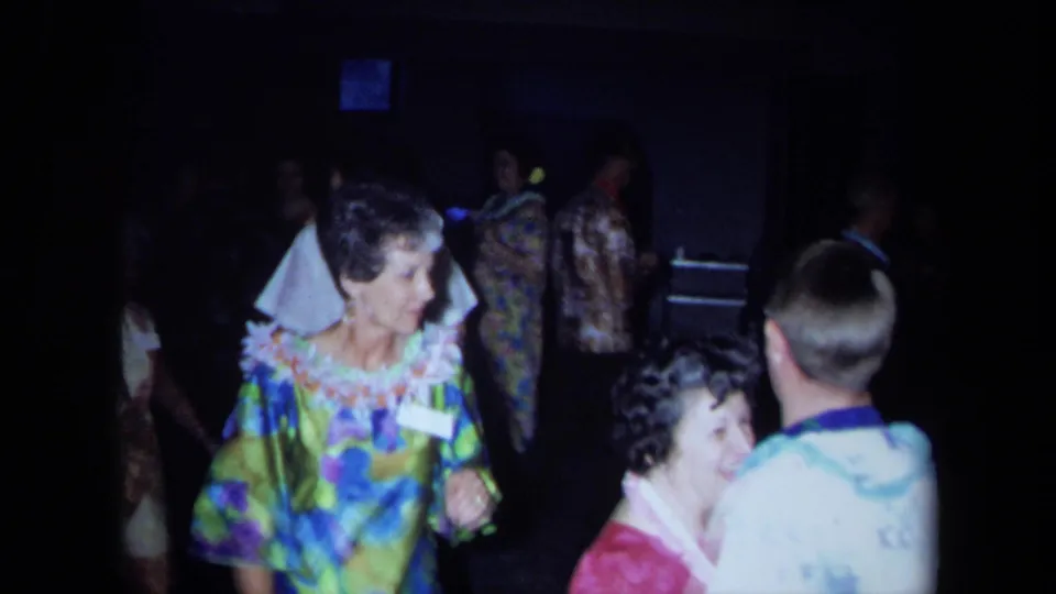 1971 California home-movie frame of adults dancing and mingling at a Hawaiian-themed indoor party.