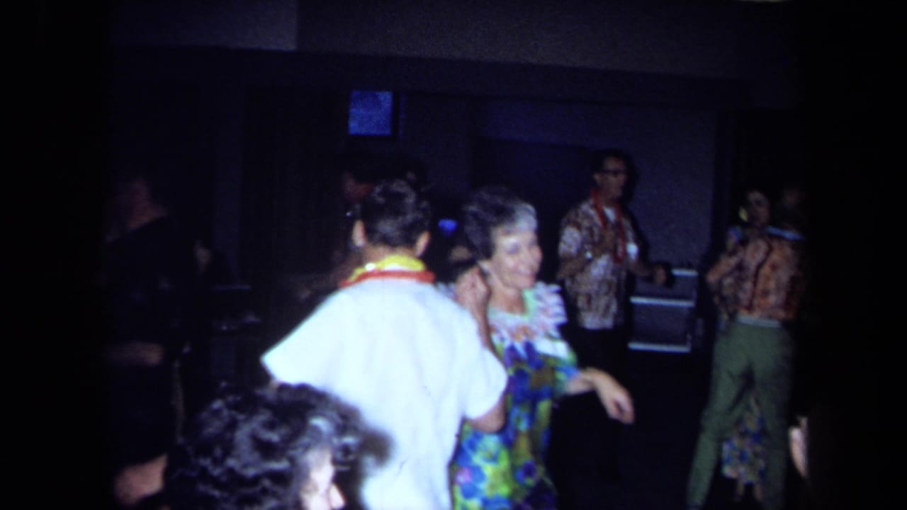 Guests wearing leis dance and socialize in a dim room.