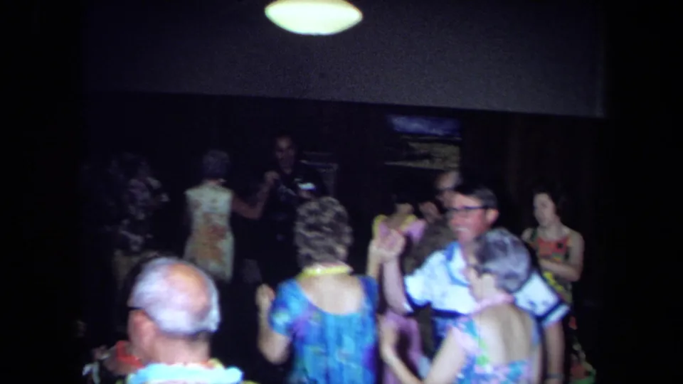 Home-movie view of a 1971 California indoor party with adults dancing under low light and wearing leis.