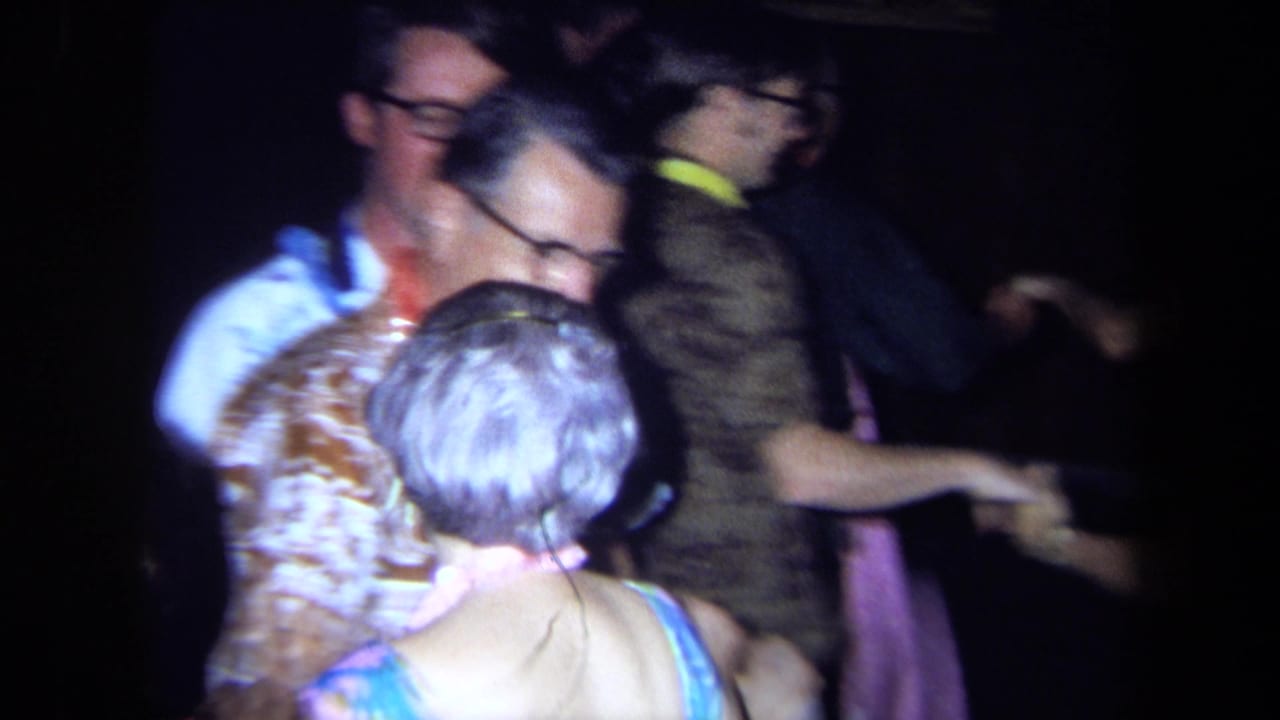 Older adults in leis and patterned clothing dancing in a dim room.