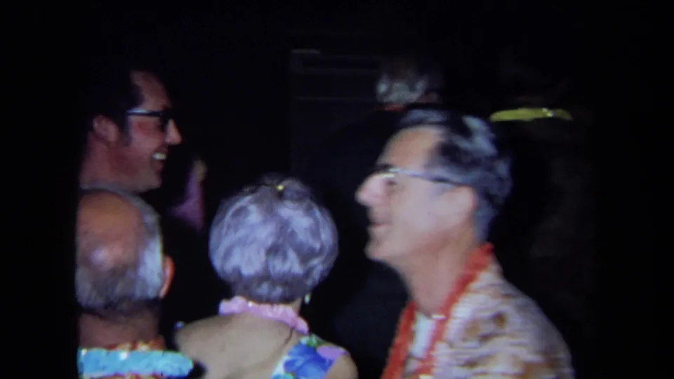 Guests at the California 1971 themed party smile and dance, with leis and aloha-style clothing visible in the dark room.