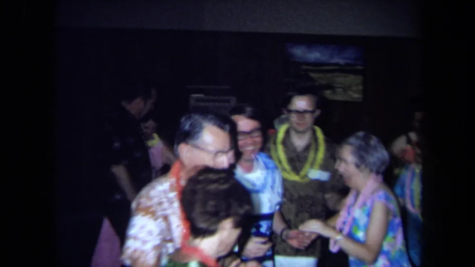 Several older adults gather and dance at the 1971 California party, with leis, patterned clothing and dim wall decor visible.