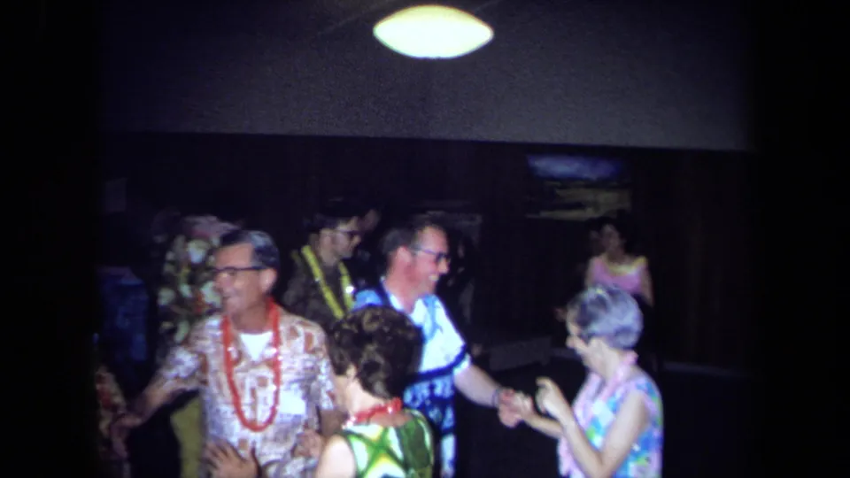Adults at a 1971 California Hawaiian-theme party wear leis and patterned clothing while dancing in a dim indoor room.