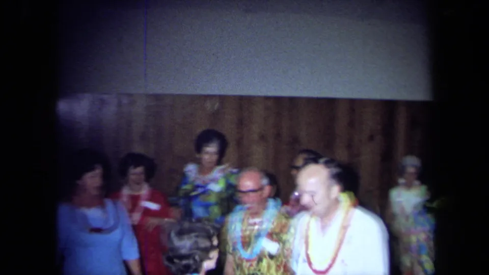 Adults in leis and colorful clothing gather near a wood-paneled wall during a 1971 California indoor party.