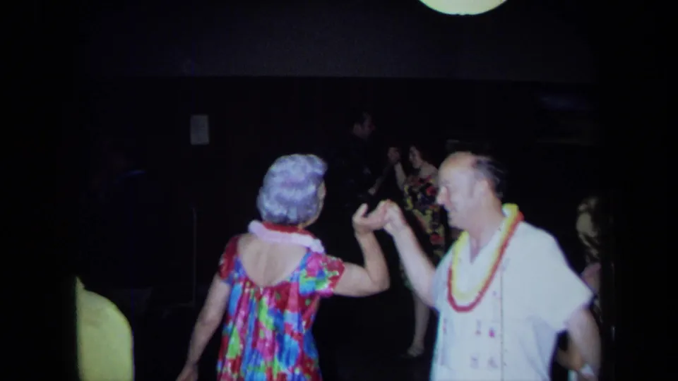 A lei-wearing pair dances hand-in-hand in the dim interior, matching the supplied 1971 California home-movie party context.