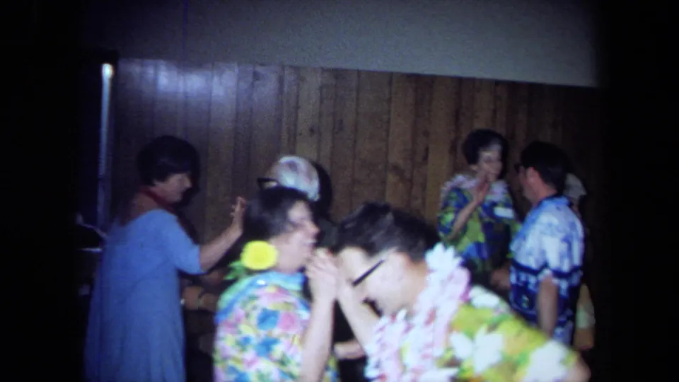 Adults at a Hawaiian-themed 1971 California party dance and talk, with leis and bright patterned clothing visible.