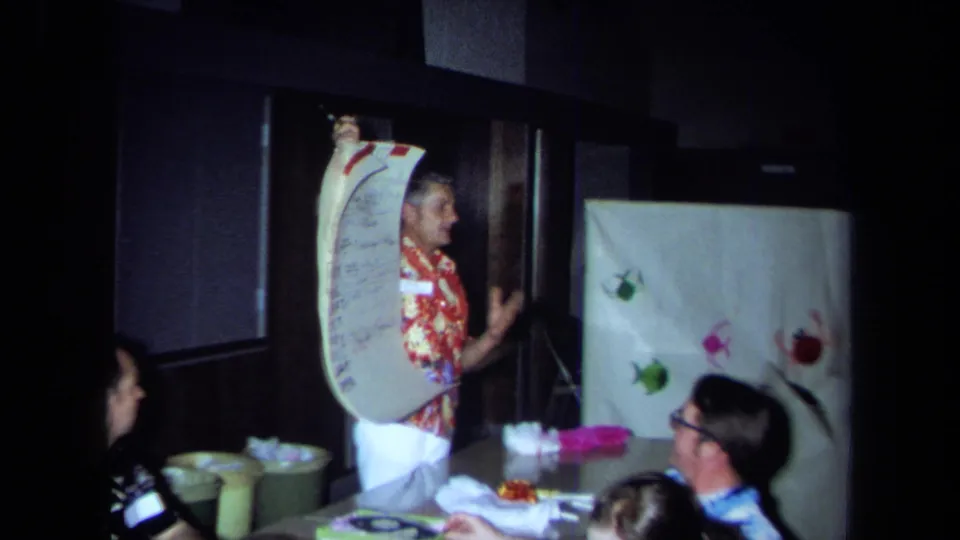A wider 1971 California frame shows the presenter beside the chart, with attendees seated at a table in a private interior.