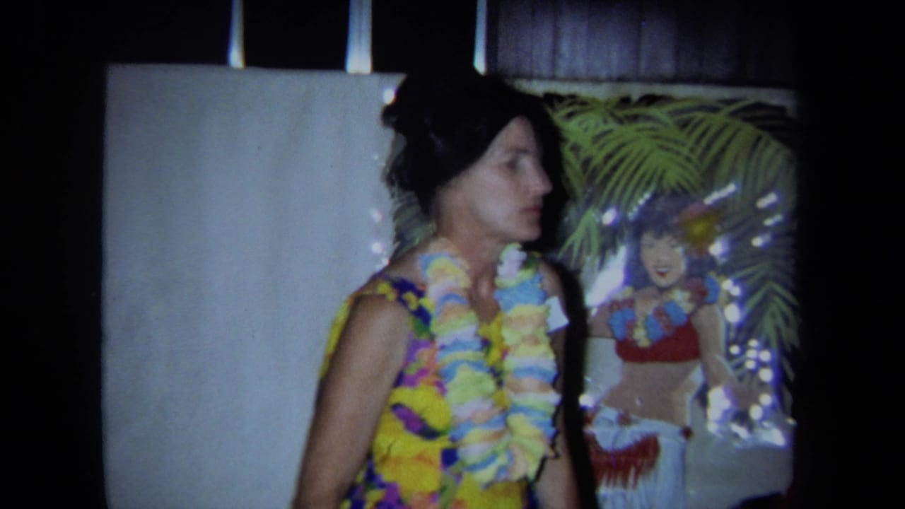 Woman wearing leis stands near tropical wall decor and a hula dancer poster.