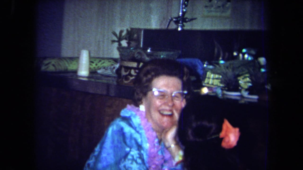Woman wearing glasses and a blue top laughs beside a bar with tropical party decor.