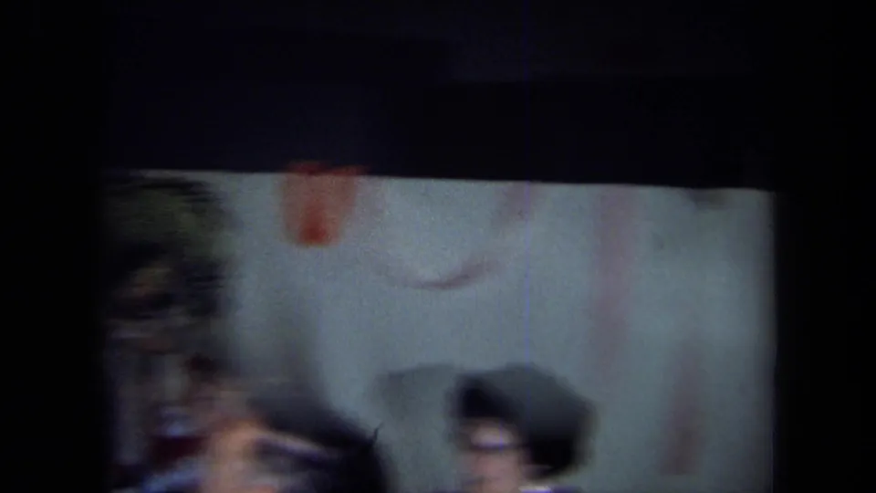 Blurred 1971 California 8mm frame showing adults moving indoors near a pale wall during the gathering.