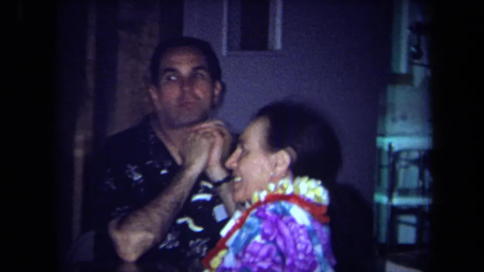 Close home-movie view of a man adjusting or holding a woman's lei during the 1971 California indoor party.