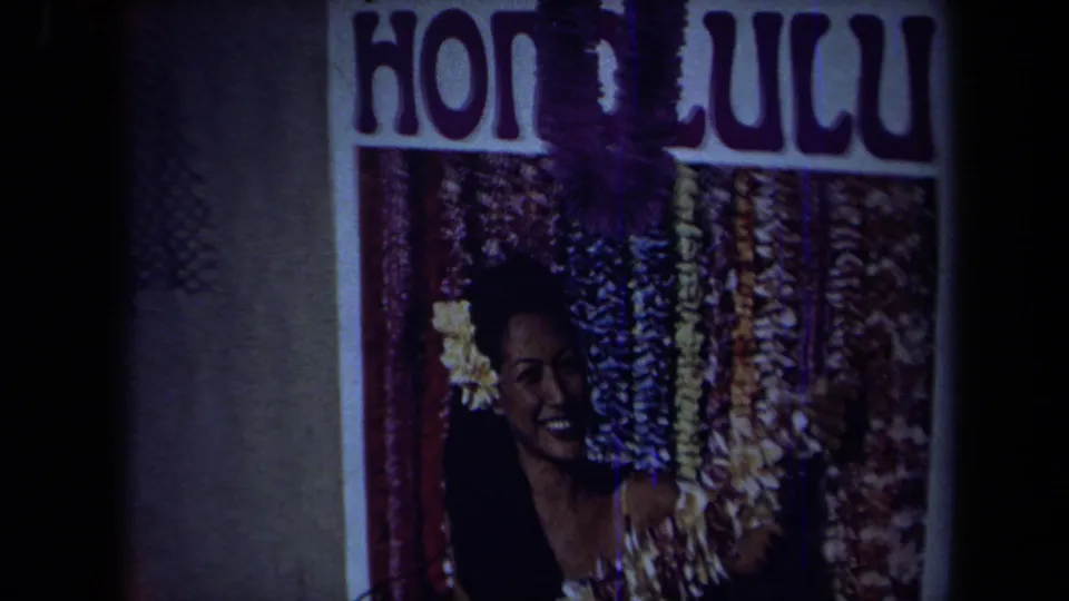 Darker 1971 California 8mm frame holds on the Honolulu poster, with the woman partly shadowed by film exposure and frame edge.