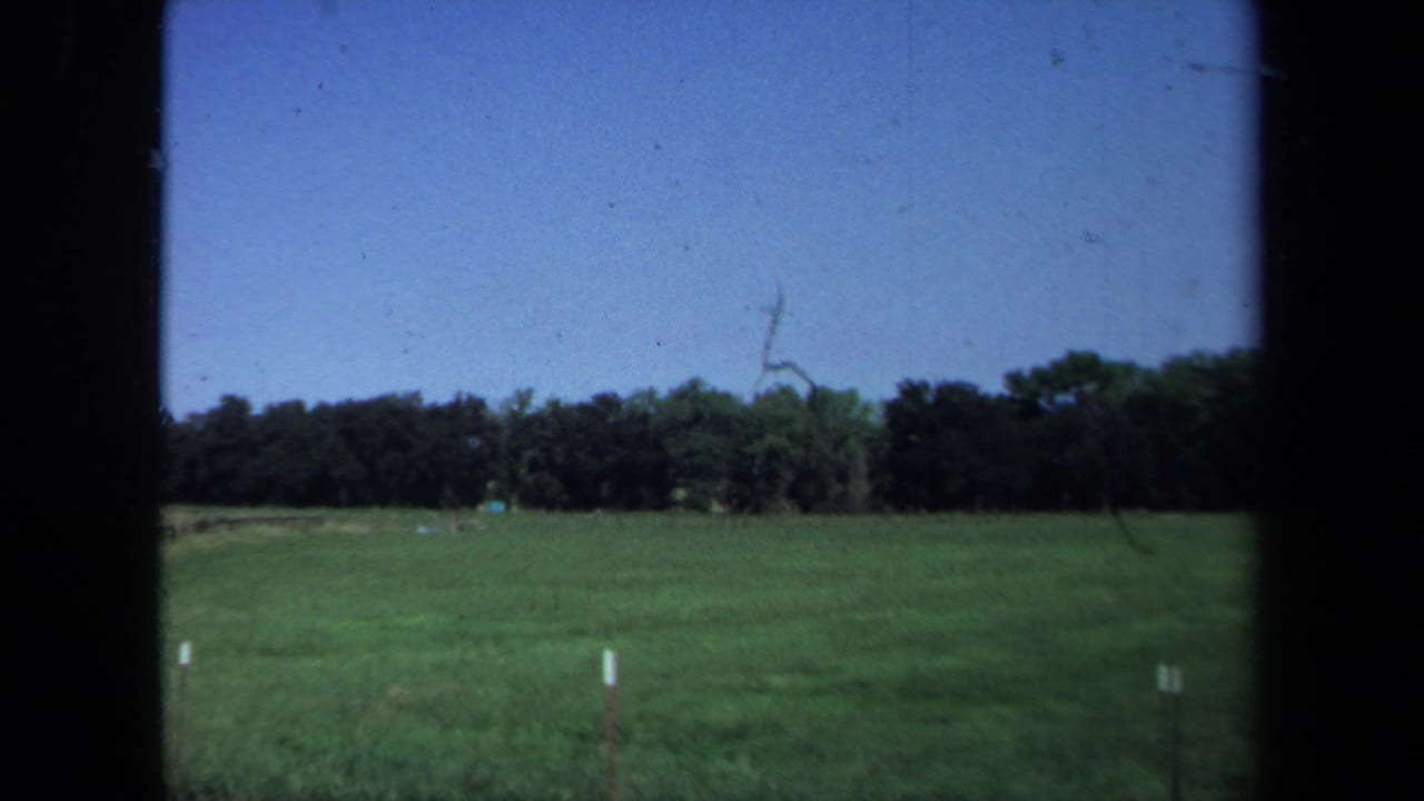 1971 California 8mm frame showing a green field, distant trees, blue sky, and dark gate borders from the film scan.