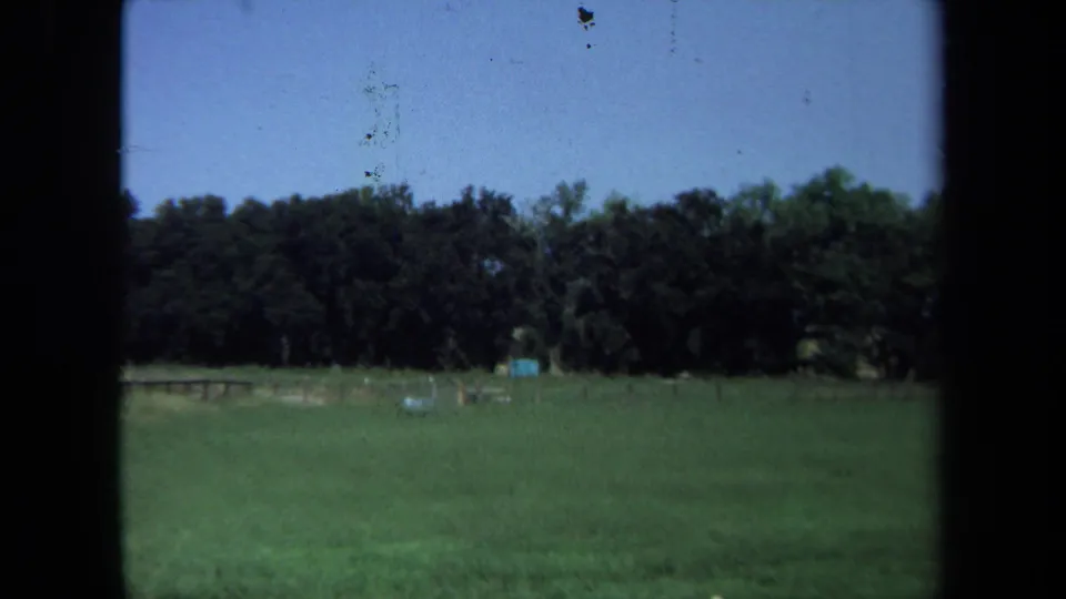 1971 California 8mm view of open grassland, a distant treeline, a small blue structure, and visible film-frame borders.