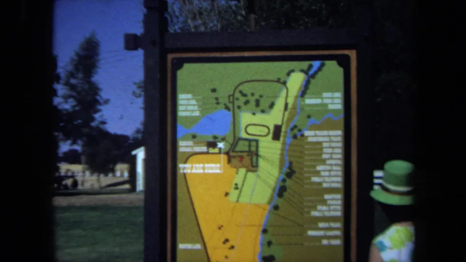 A closer 8mm frame shows the colorful park map sign, with the woman in a green hat partly visible at the edge.