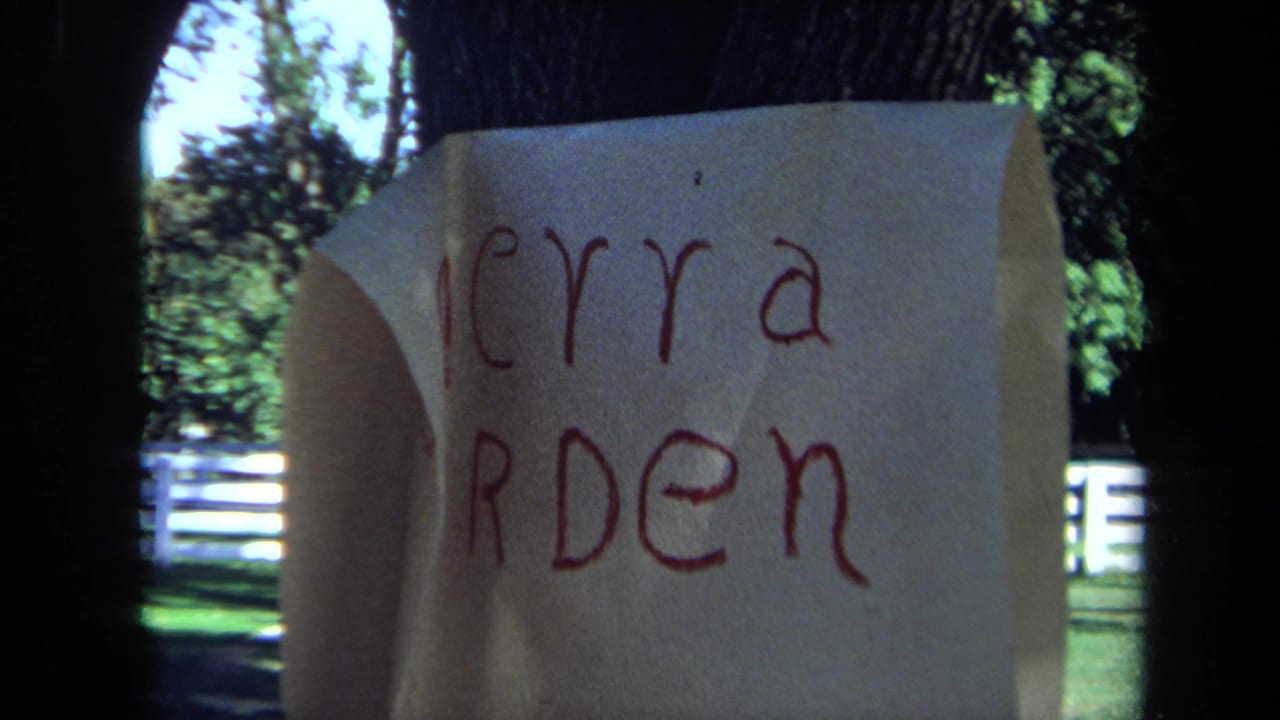 1971 California 8mm frame with a handwritten Merry Garden note in the foreground and park trees and white fencing behind it.
