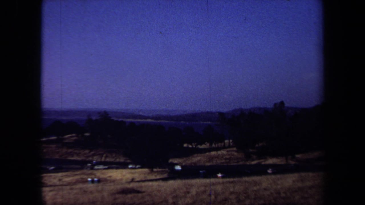 1971 California home-movie view across dry rolling countryside toward a distant body of water beneath a blue sky.