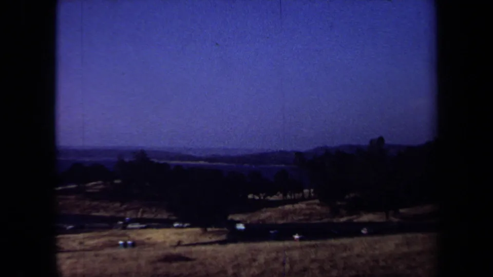1971 California home-movie view across dry rolling countryside toward a distant body of water beneath a blue sky.