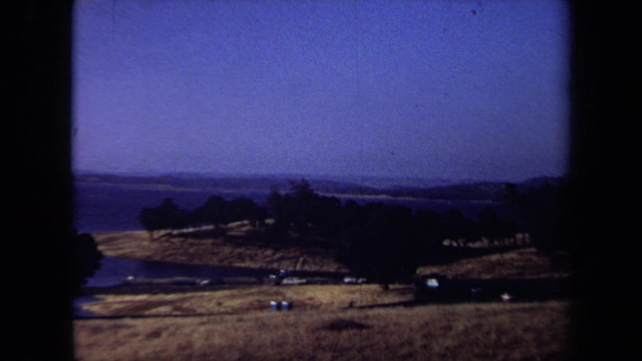 Rural hills and trees beside a distant body of water under a deep blue sky.