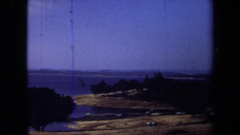 1971 California 8mm frame looking over trees and dry grassland toward a wide blue water surface.