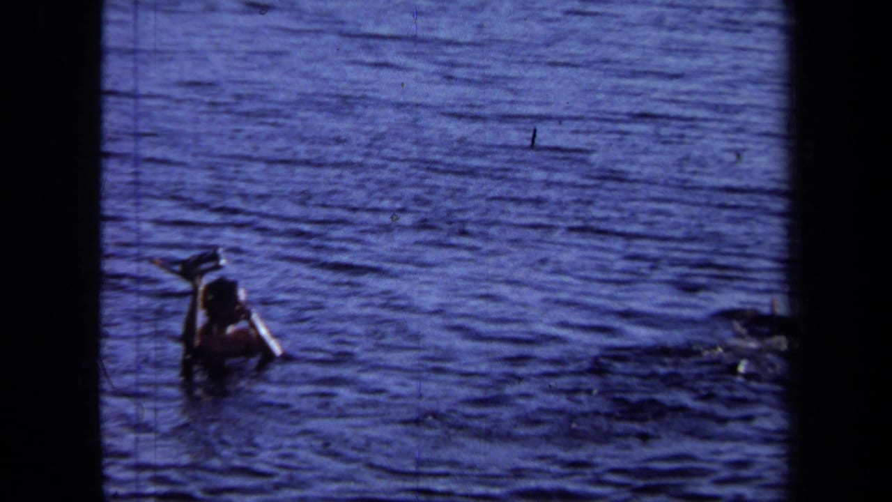 In 1971 California home-movie footage, a person swims in deep blue water while holding what appears to be a camera above the surface.