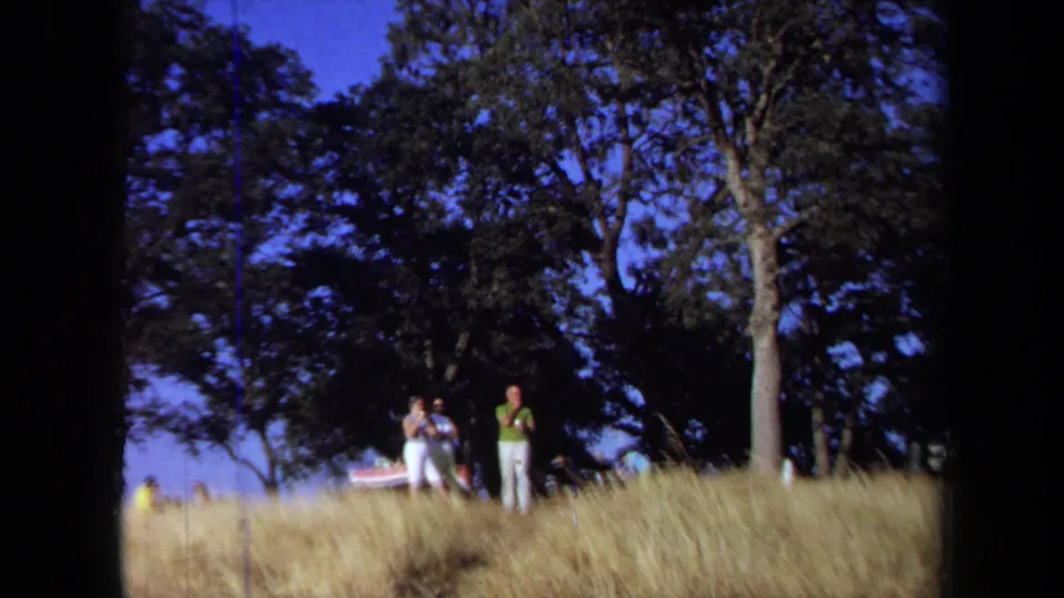 A small group stands on a dry grassy hillside beneath trees, likely near the same California water outing shown in the clip.